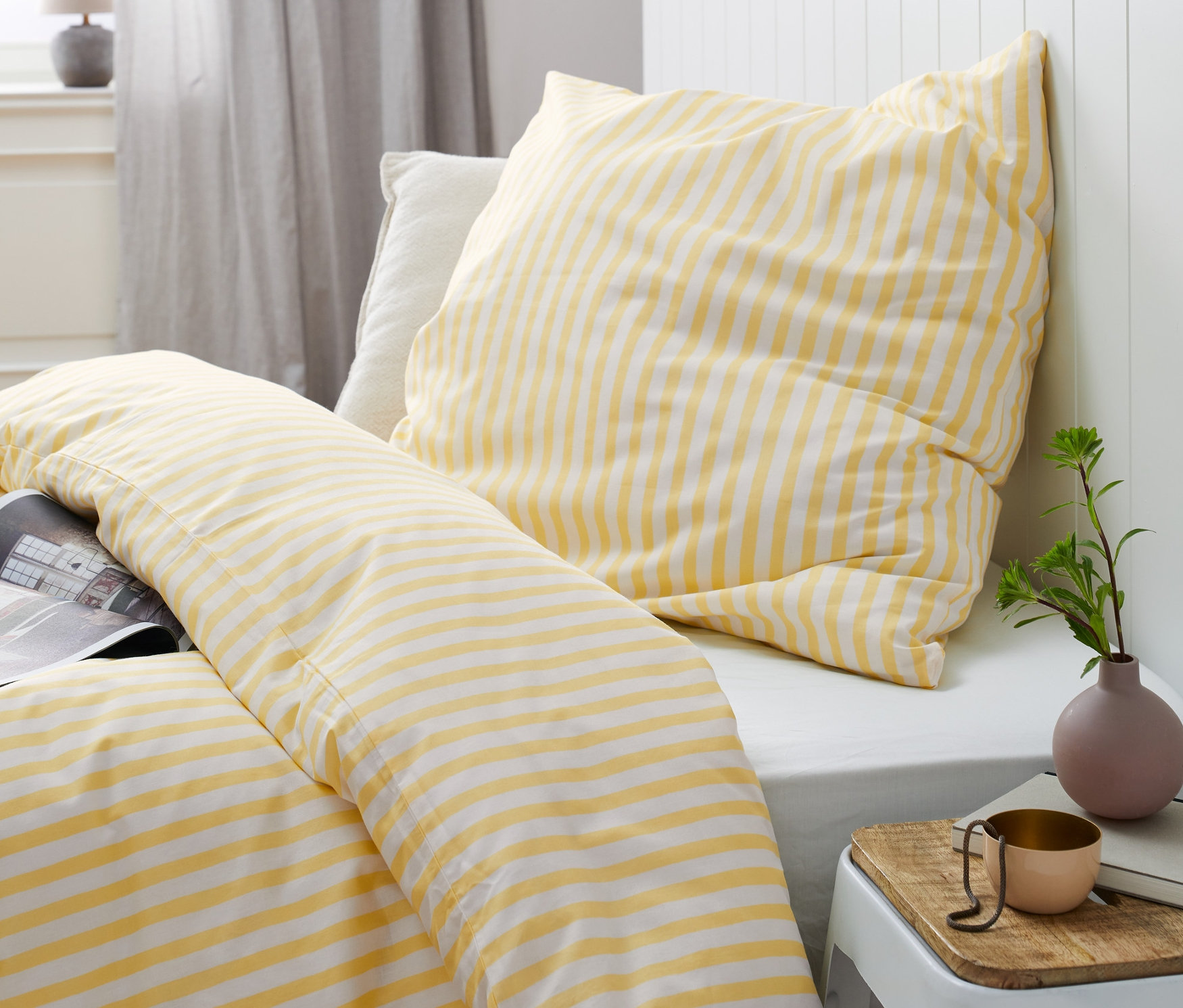 Gelb-weiß gestreifte Renforcé-Bettwäsche in verschiedenen Größen auf einem Bett.