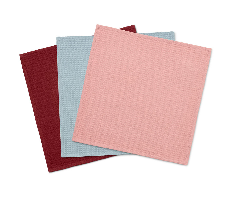 Drei Küchenhandtücher liegen übereinander: eines ist bordeauxrot, eines hellblau und eines rosa.