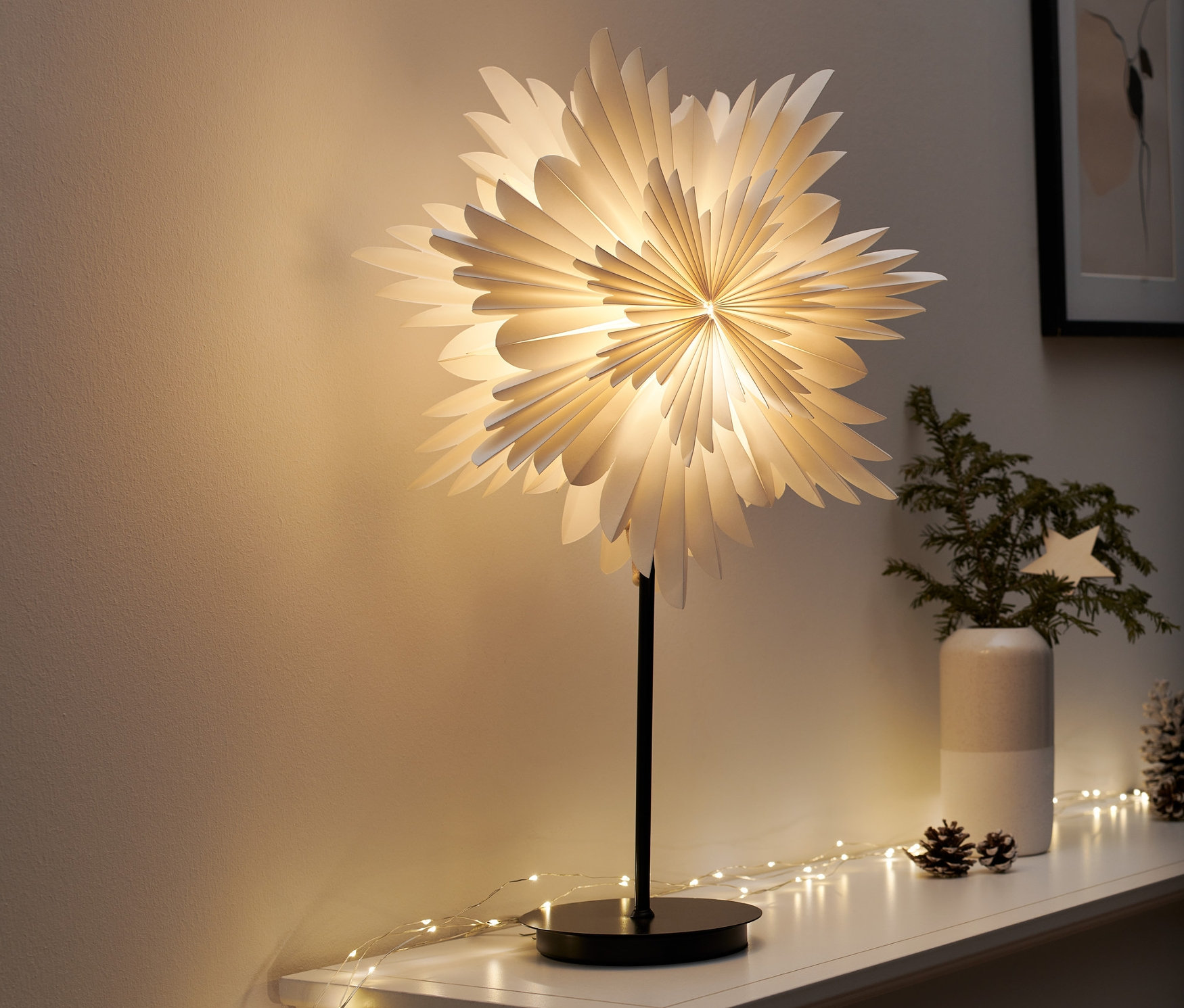 Eine LED-Dekoleuchte »Stern« steht auf einem weißen Regal. Darum herum sind Lichterketten und Weihnachtsdekoration.