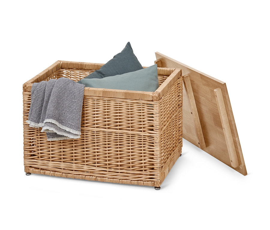 Eine Truhe aus Geflecht mit blauen Kissen, einer grauen Decke und einem geöffneten Holzdeckel.