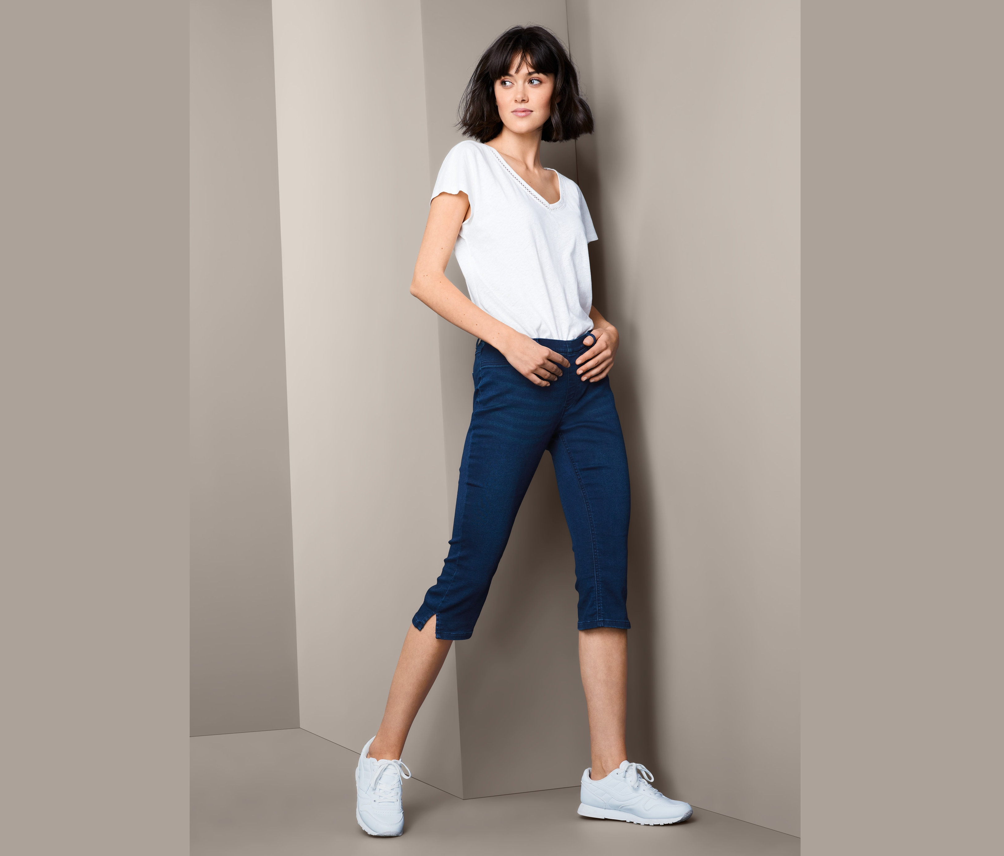 Frau posiert in weißem T-Shirt und 3/4-Jeggings.