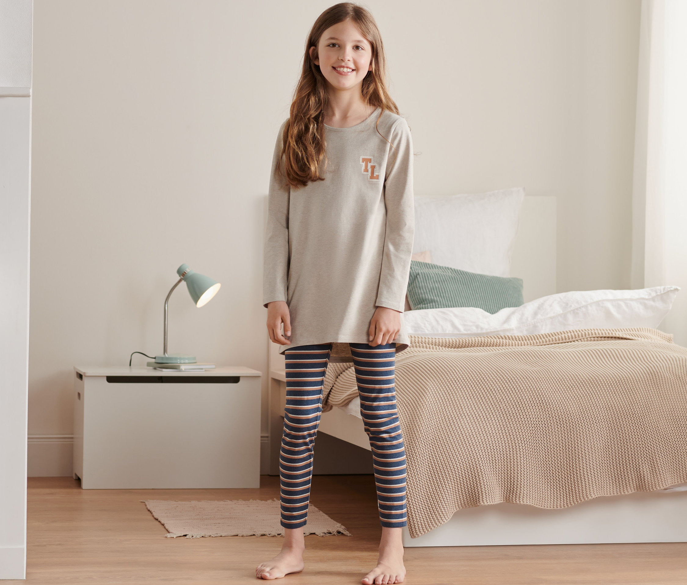 Mädchen steht in einem Kinderpyjama mit gestreiften Leggings.