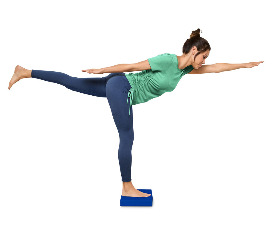 Frau steht auf Balance-Pad und macht Yoga-Pose.