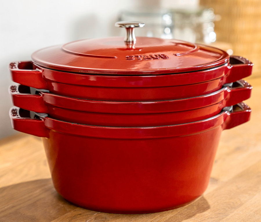 Auf einer Holzfläche sind drei rote STAUB Kochtopf-Set »La Cocotte« gestapelt.