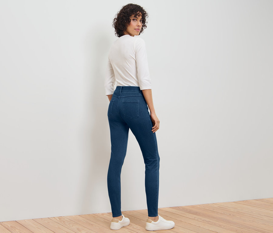 Eine Frau blickt über ihre Schulter und trägt Jeggings, ein weißes Shirt und weiße Turnschuhe.