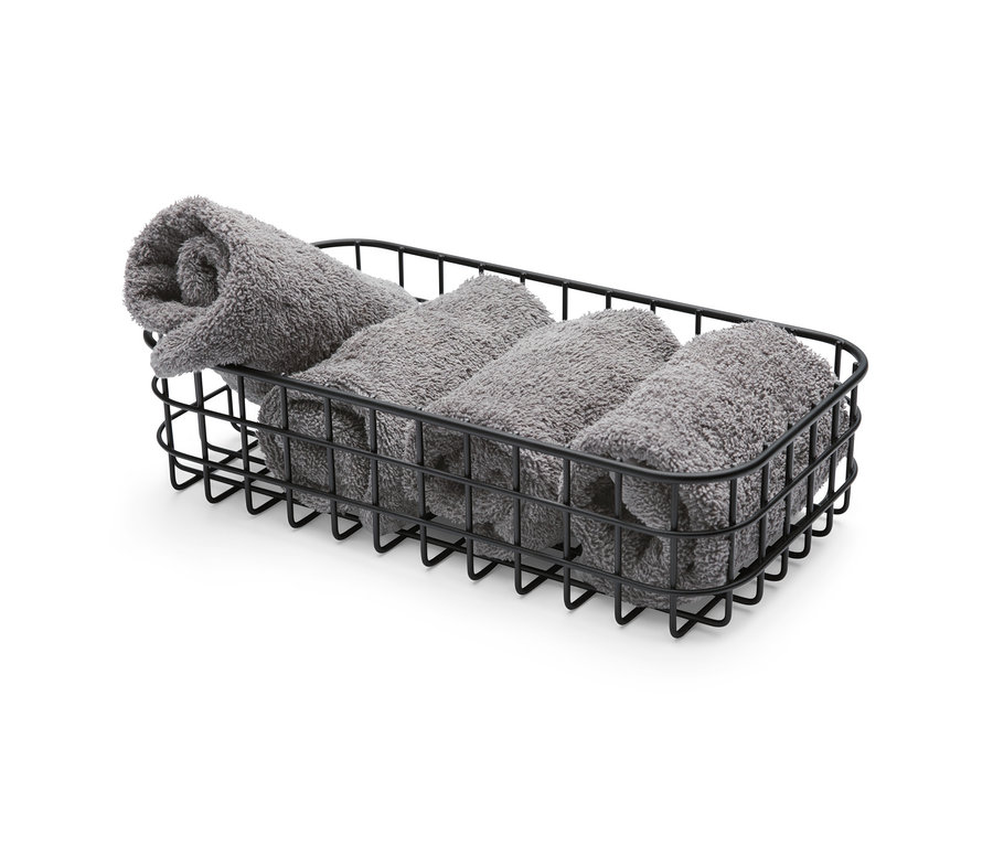 Vier graue Handtücher sind ordentlich in einem schwarzen Aufbewahrungskorb aufgerollt.