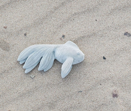 Helles blaues Dekoobjekt Fisch »Mike« liegt im Sand.