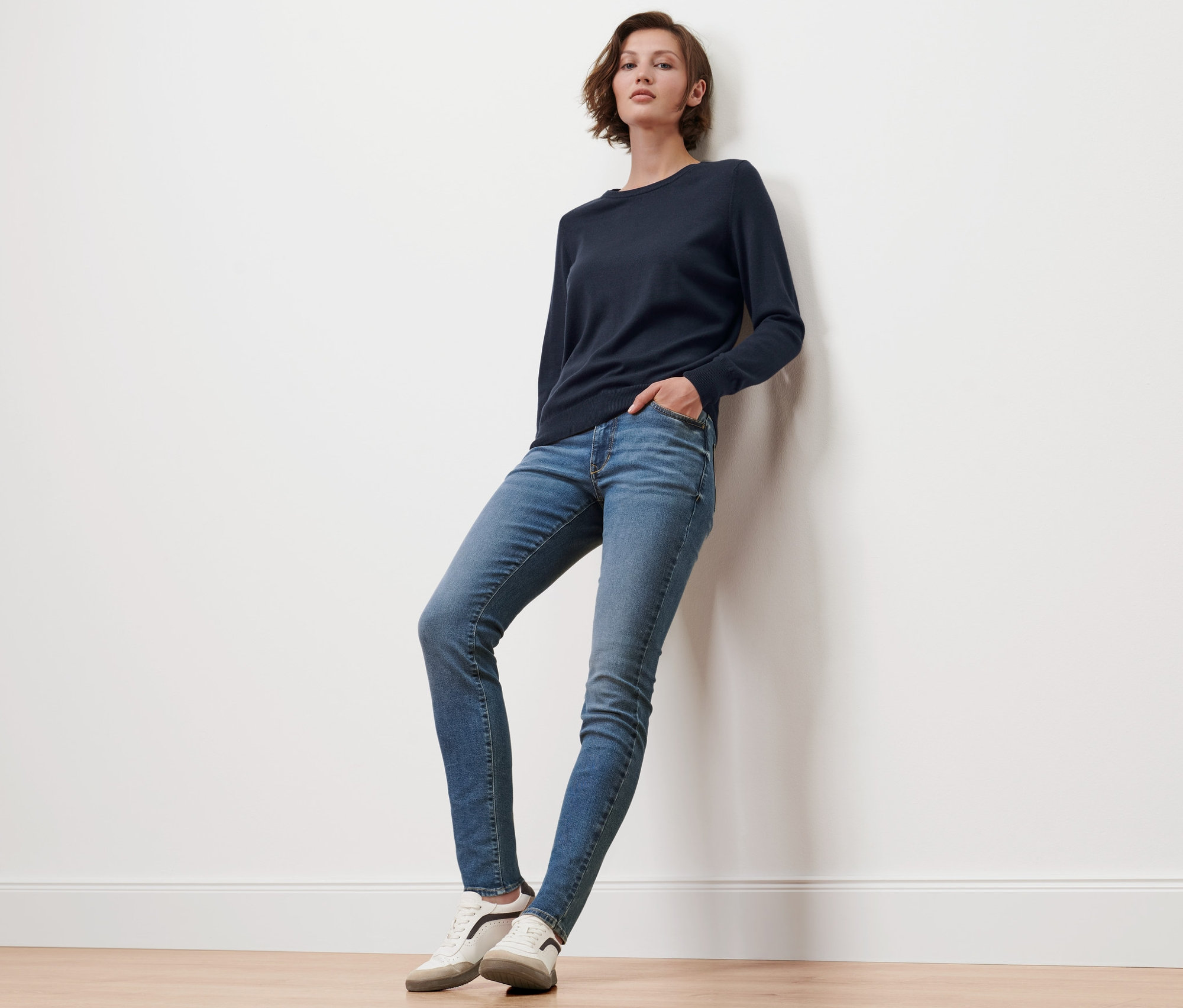 Frau lehnt an Wand und trägt dunkelblauen Merino-Feinstrickpullover.