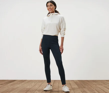 Eine Frau steht auf einem Holzboden und trägt Heavy-Leggings und ein Sweatshirt.