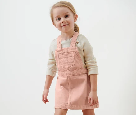Lächelndes blondes Mädchen im Kinder-Latzkleid.