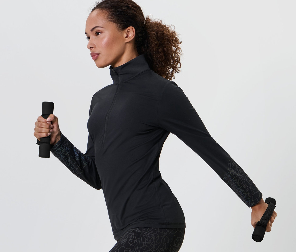 Frau in schwarzer Sportbekleidung hält je eine 2 Lauf-und-Gymnastikhanteln in jeder Hand.