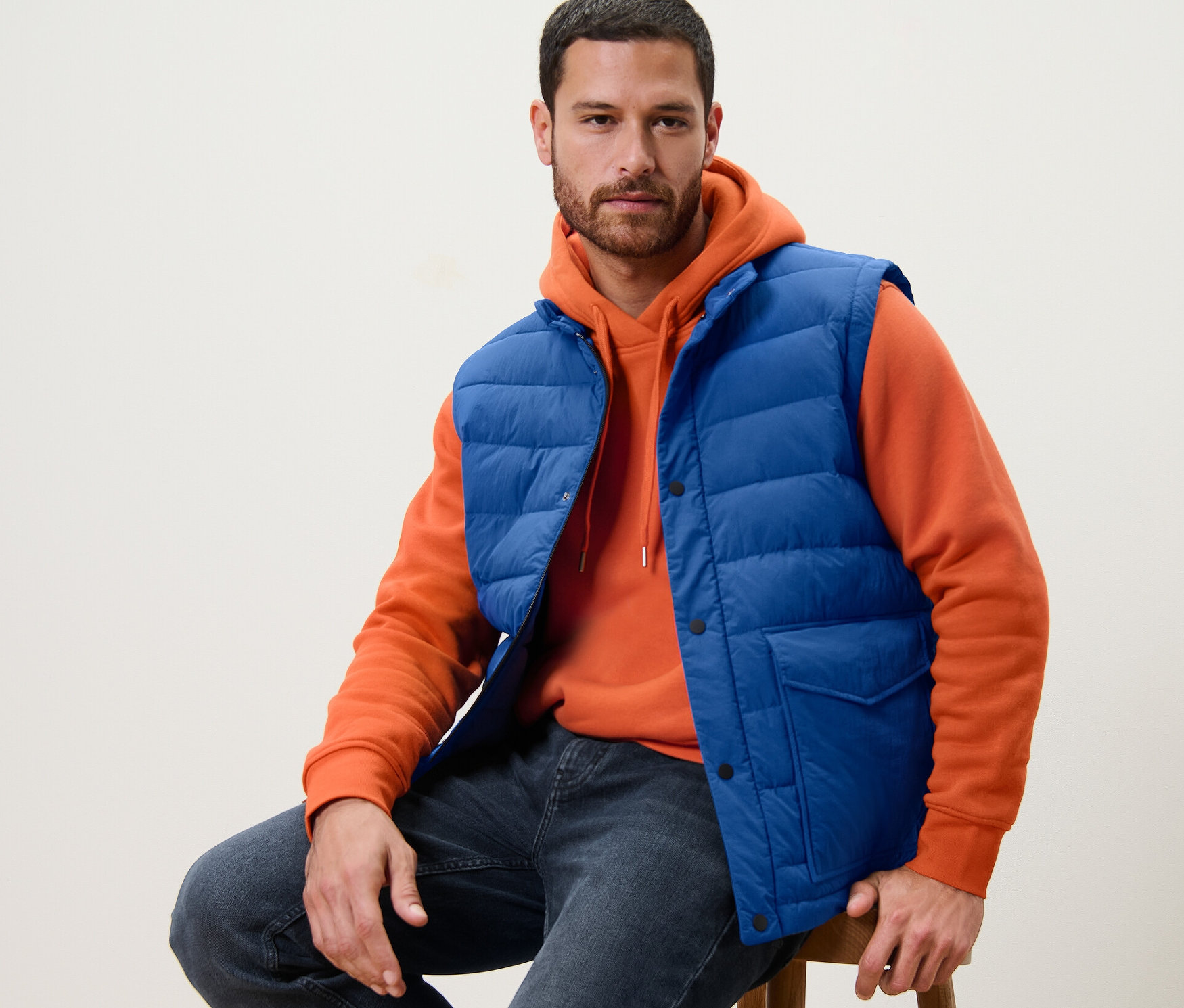 Mann sitzt auf einem Hocker und trägt eine blaue Steppweste.