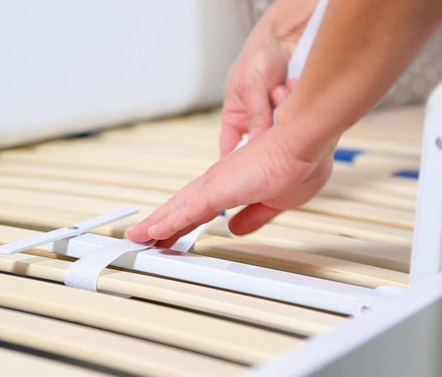 Eine Hand befestigt ein graues roba Bettschutzgitter »Klipp-Klapp« an einem Bett.