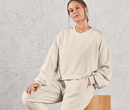 Eine Frau sitzt auf einem Holzhocker und trägt einen extraweichen Sweatpullover und eine extraweiche Sweathose.