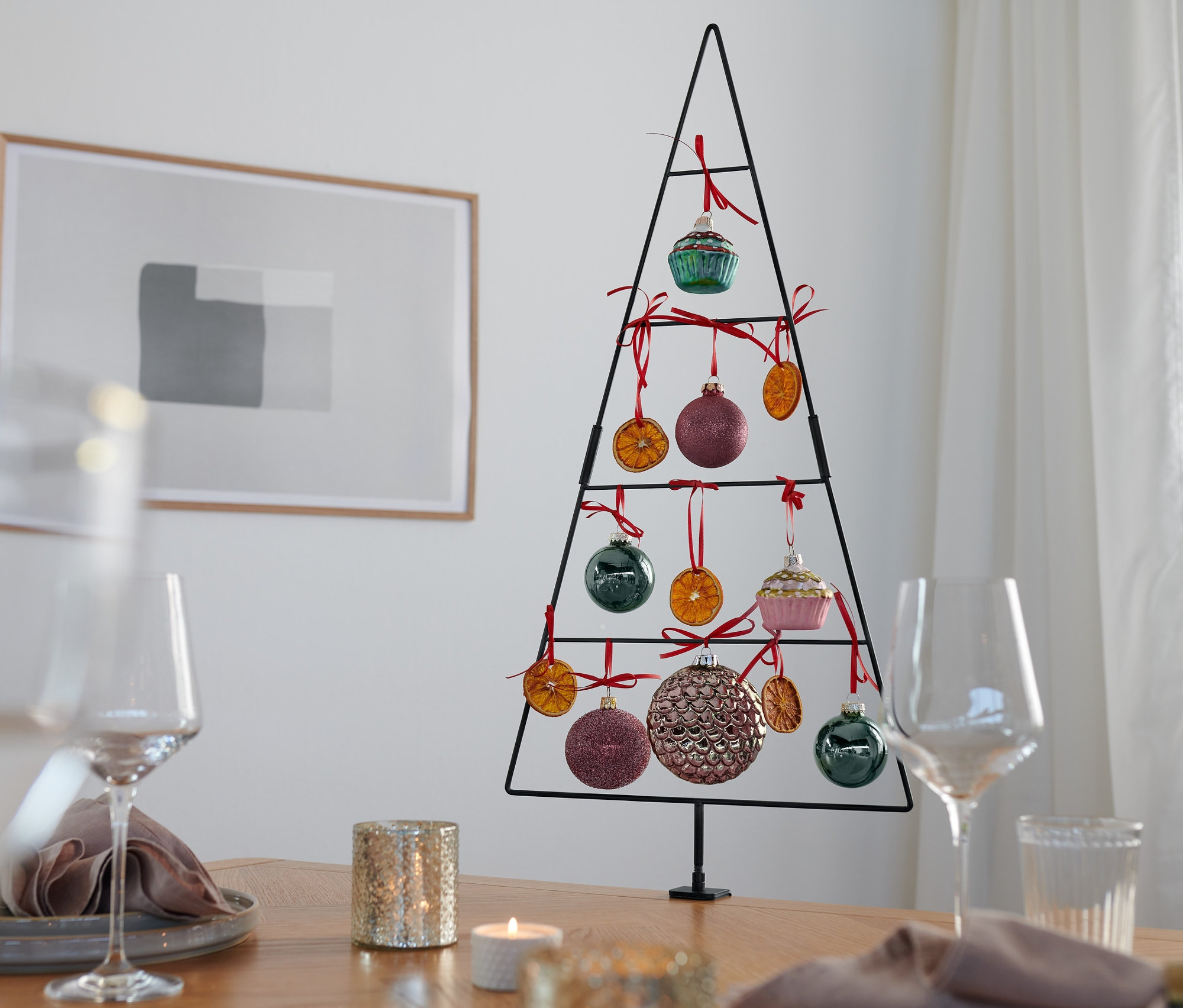 Ein Deko-Tannenbaum steht auf einem Tisch, geschmückt mit Ornamenten und getrockneten Orangen.