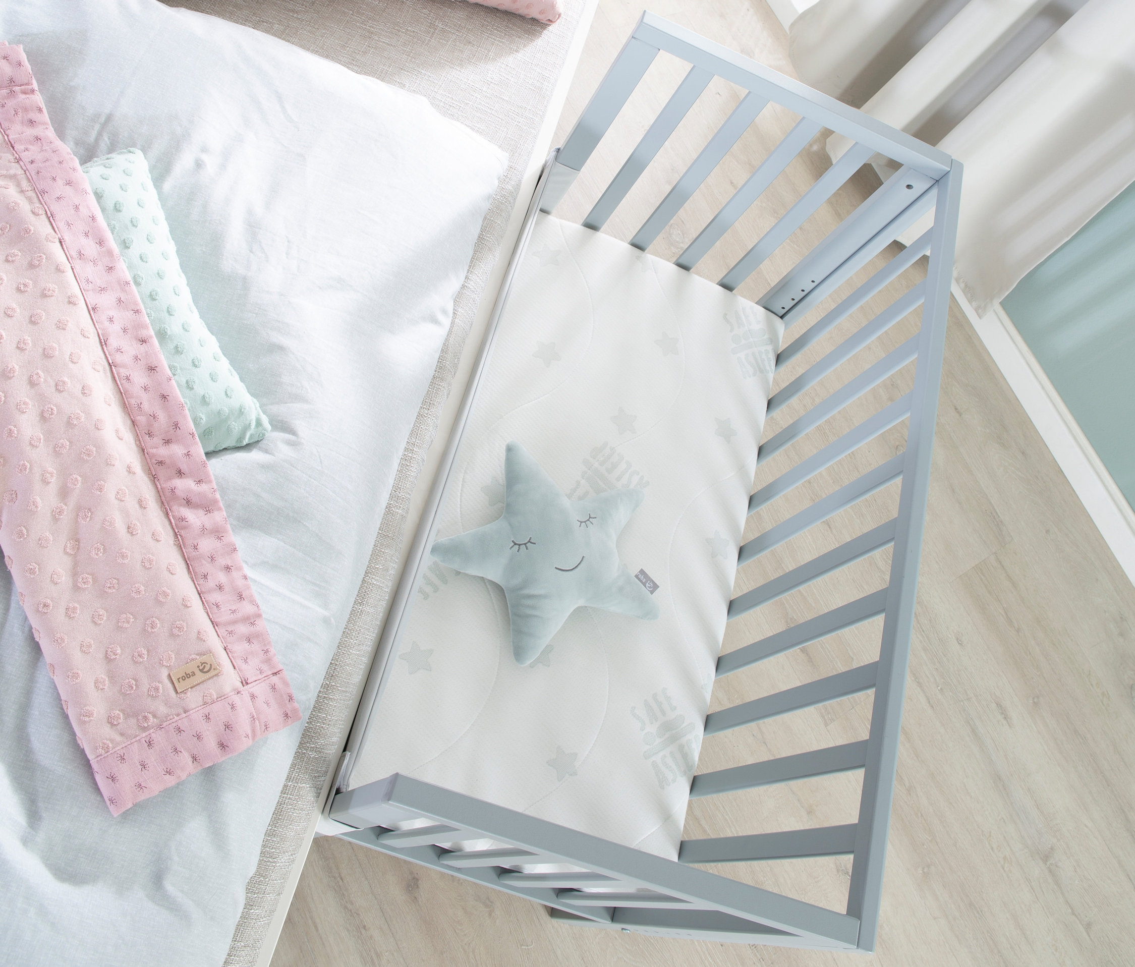 Draufsicht auf roba 2-in-1-Beistellbett »safe asleep®«, taupefarben, mit Stern, und Bett mit rosa Kissen.