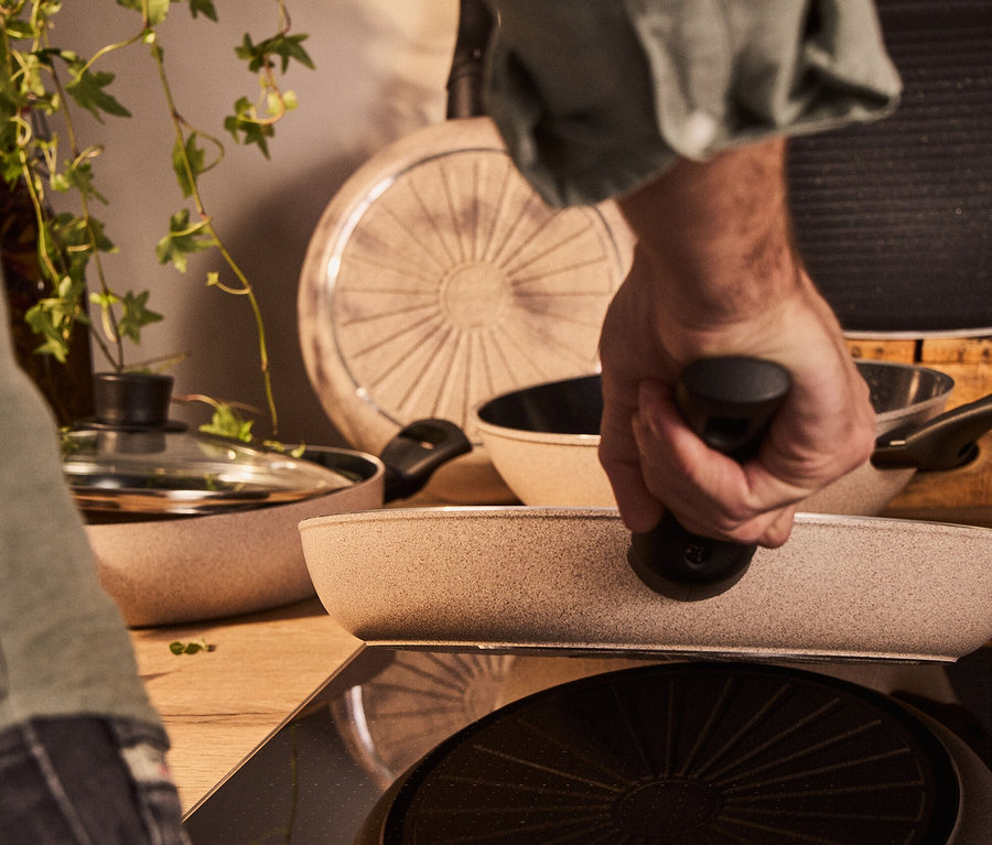 Mann hält eine sandfarbene BALLARINI Aluminium-Bratpfanne, 24 cm, auf einem Herd.