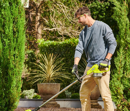 Ein Mann trimmt mit einem RYOBI 18 V One+ Akku-Rasentrimmer mit Radführung den Rasen.