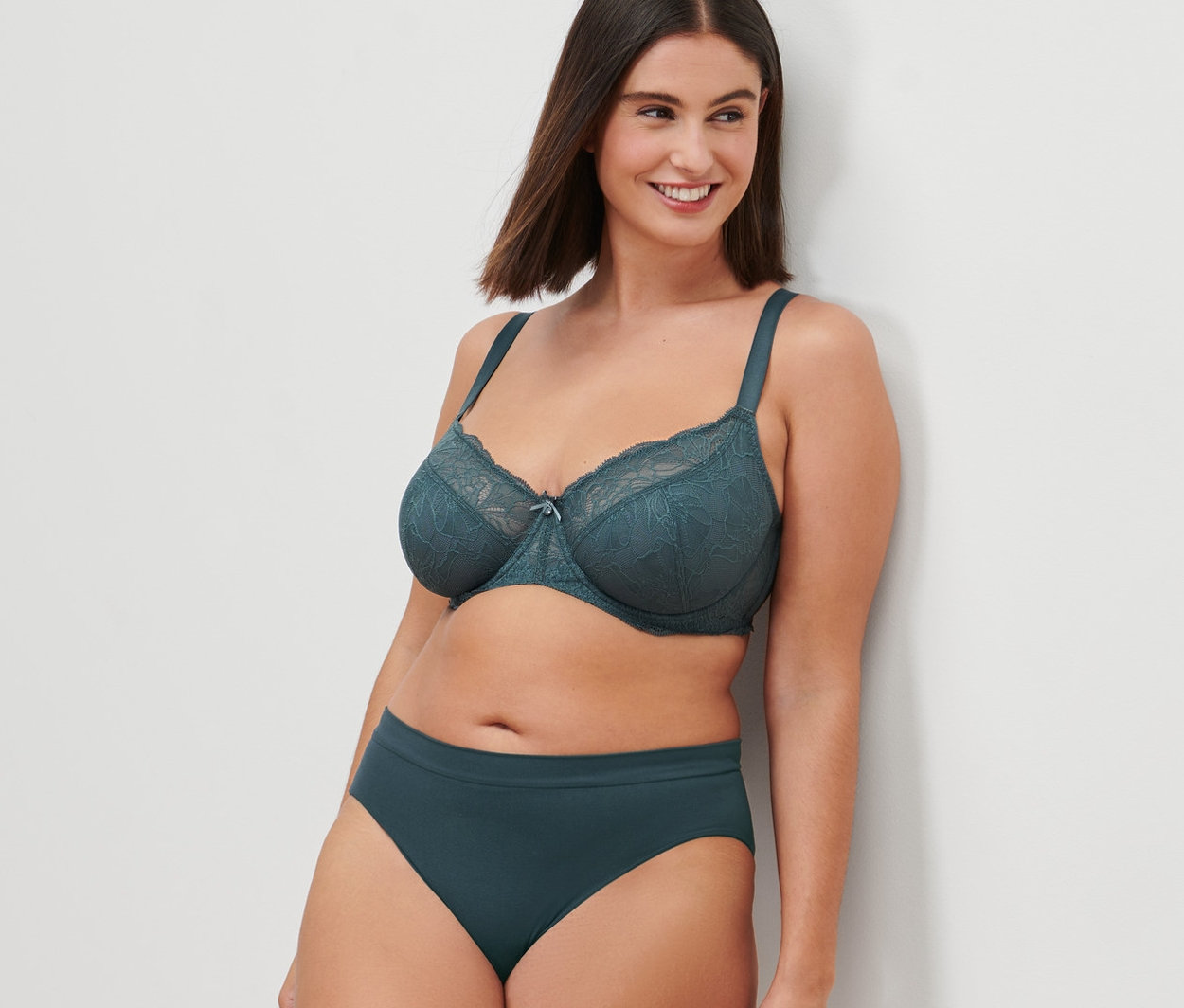 Frau an eine Wand gelehnt, trägt einen Bügel-BH und Unterhose.