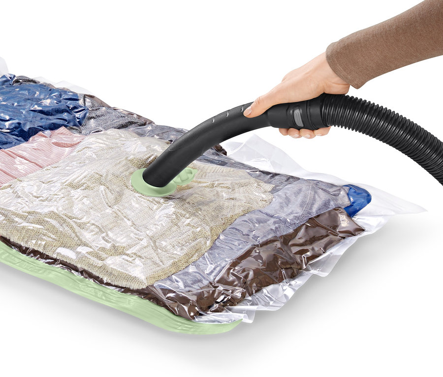 Eine Hand benutzt eine Vakuumpumpe auf einem liegenden Vakuum-Aufbewahrungsbeutel mit Kleidung.