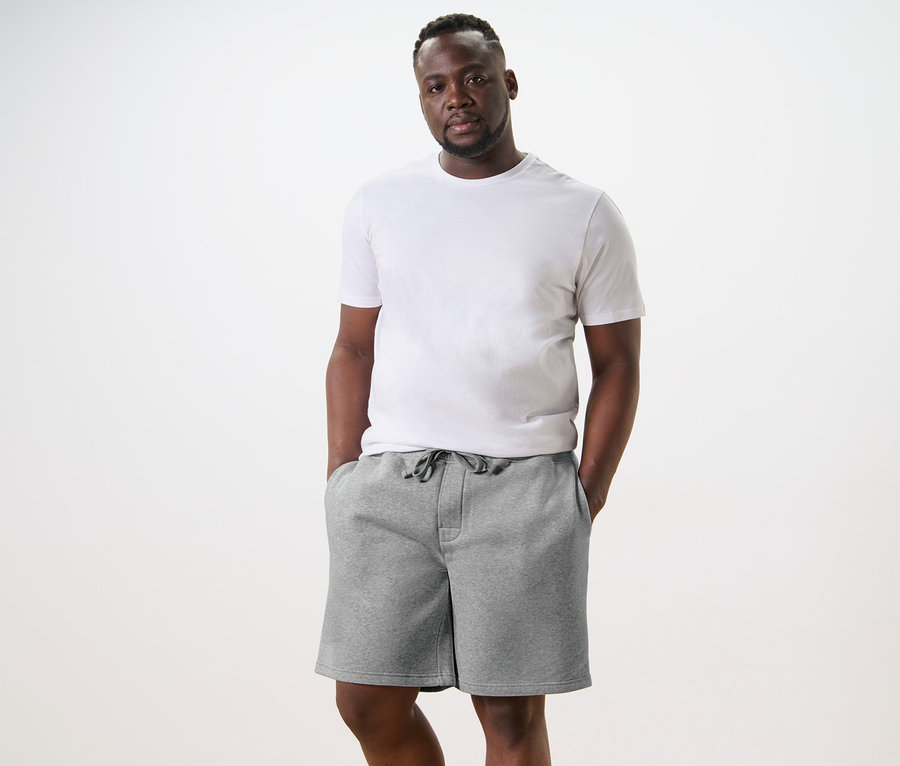 Mann steht mit Händen in den Taschen der hellgrauen Sweatshorts.