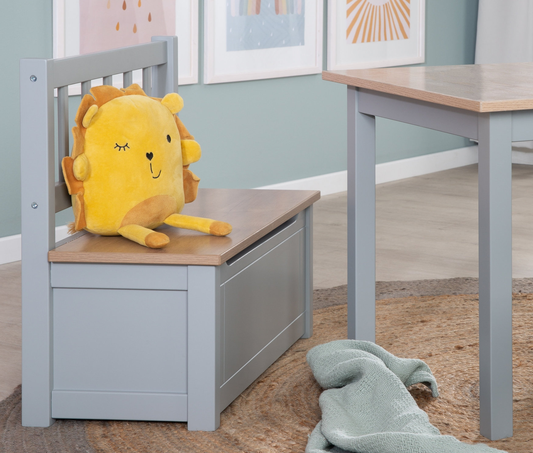 Gelbes Löwenkuscheltier sitzt auf roba Kindertruhenbank »Woody« neben Tisch auf Jute Teppich.