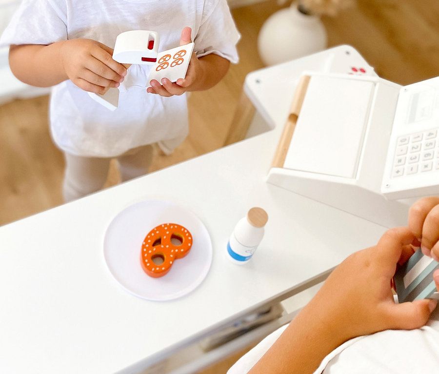 Mädchen hält Spielzeugkasse und Brezelkarte, während Junge an small foot Kasse »fresh« steht.