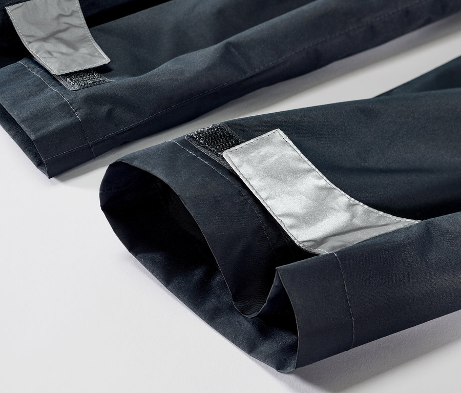 Detailaufnahme einer Kinder-Regenhose mit Reflektoren und Klettverschluss am Saum.