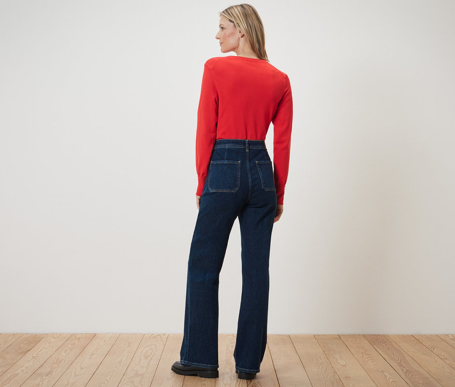 Eine Frau posiert mit dem Rücken zur Kamera und trägt eine Flared Jeans – Fit »Cara« und ein rotes Oberteil.