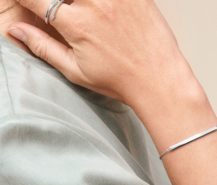 Profil einer Frau mit braunen, zum Pferdeschwanz gebundenen Haaren. Sie trägt Doppel-Creolen aus 925er Silber mit Zirkonia, einen Ring Pfeil mit Zirkonia und ein Armband Identität.