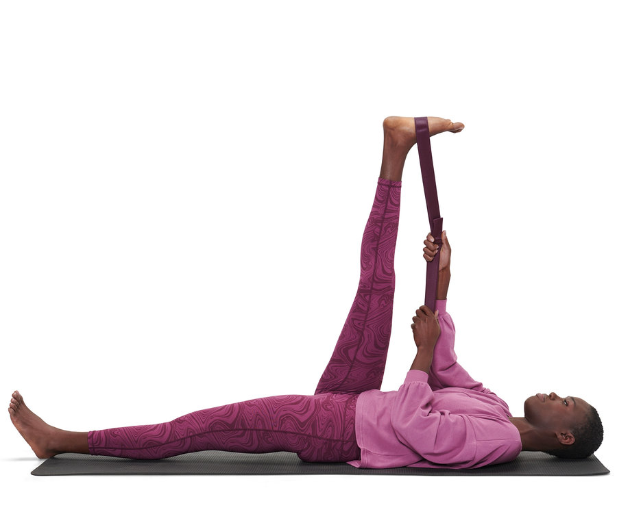 Eine Frau liegt auf einer Matte und dehnt ihr Bein mit einem 2-in-1-Yogagurt.