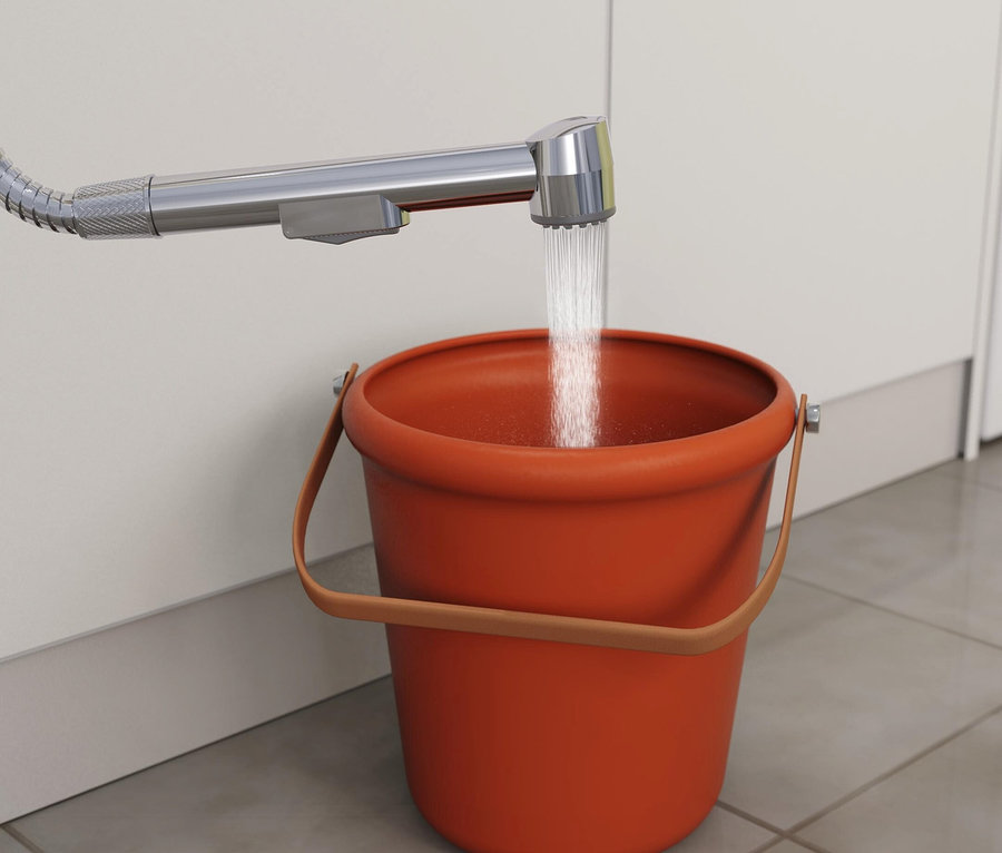 Wasser fließt aus einem verchromten Duschkopf in einen orangefarbenen Eimer.