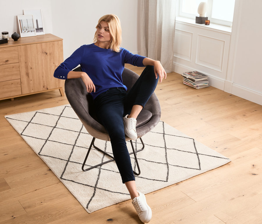 Frau sitzt im Sessel und trägt eine Samthose.