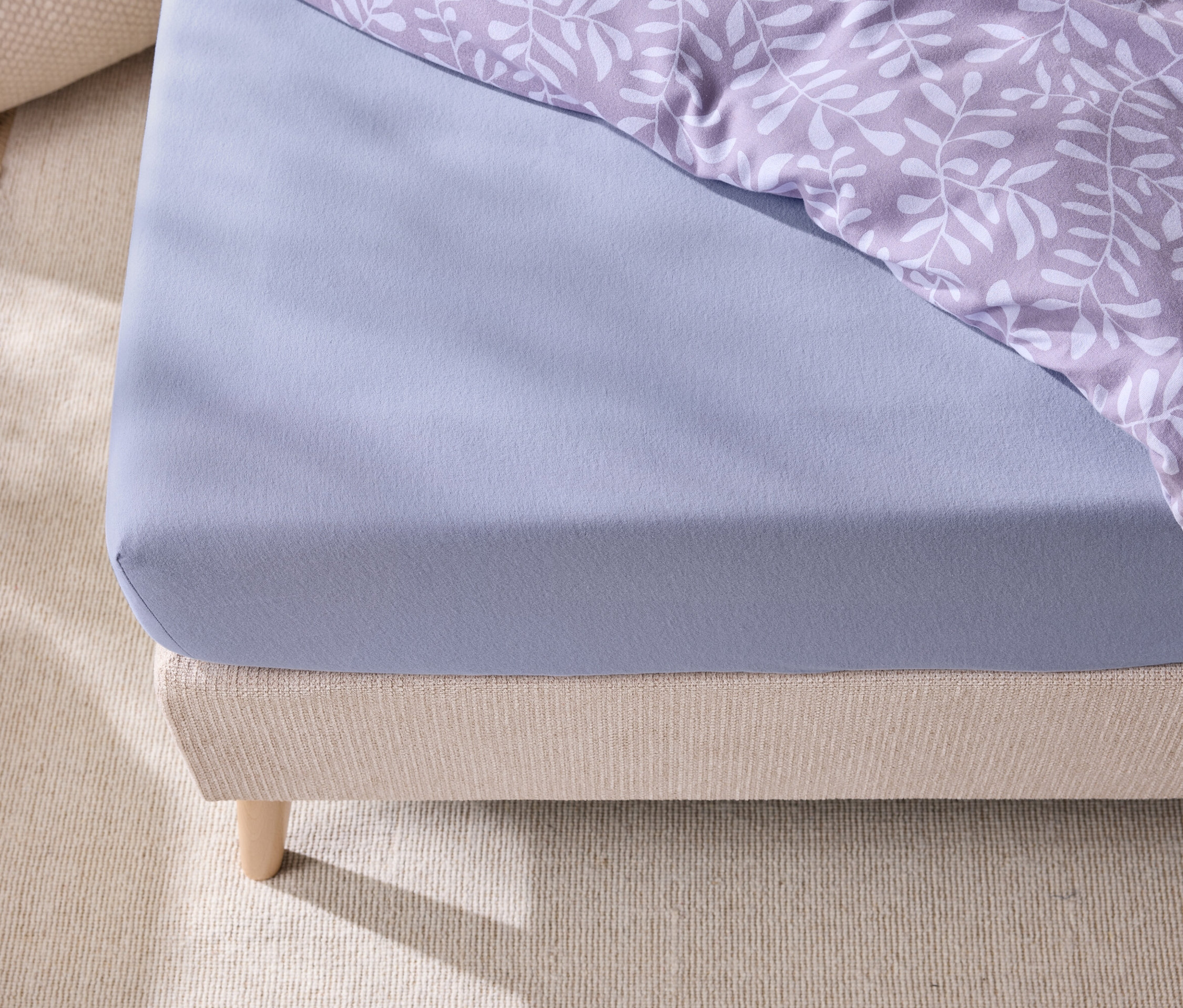 Detailansicht eines Bettes mit einem blauen Spannbettlaken und Bettwäsche mit Blattmuster.