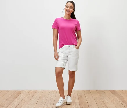 Eine Frau posiert in cremeweißen Denim Shorts ‒ Fit »Lea« und einem pinken T-Shirt.