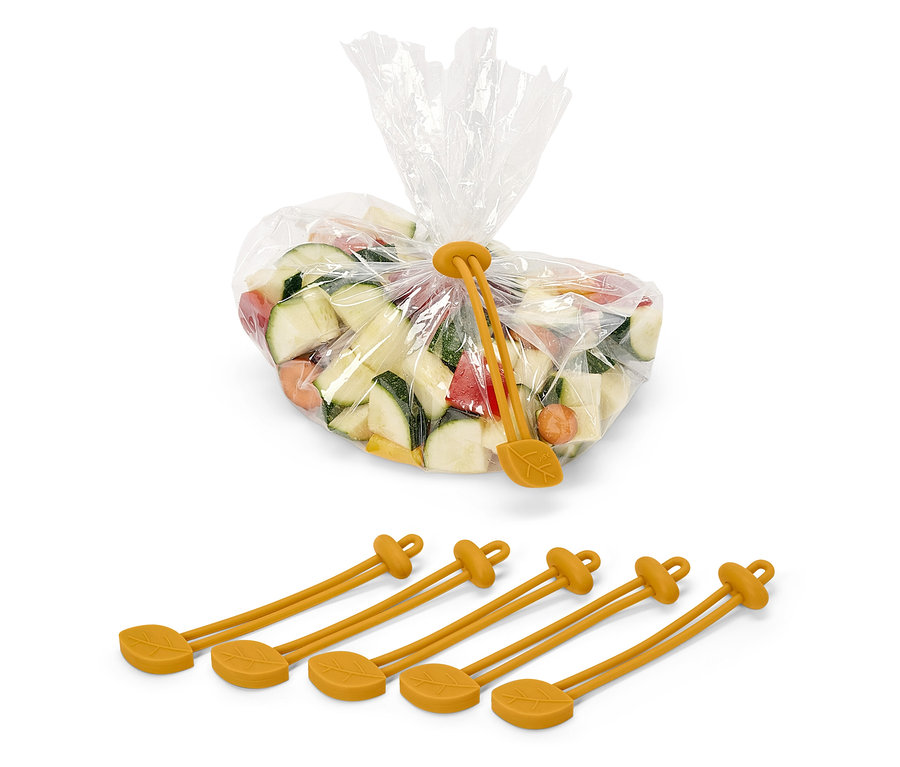 Gehackte Zucchini, Karotten und Paprika in einem Plastikbeutel, der mit einem gelben Silikonband mit Blattmotiv verschlossen ist. Unter dem Beutel befinden sich vier gelbe Silikonbänder.