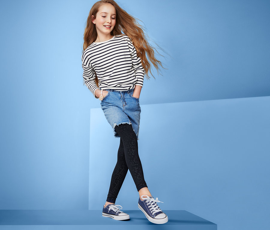 Mädchen steht auf blauem Sockel und trägt Thermoleggings, Jeansrock und gestreiftes T-Shirt.