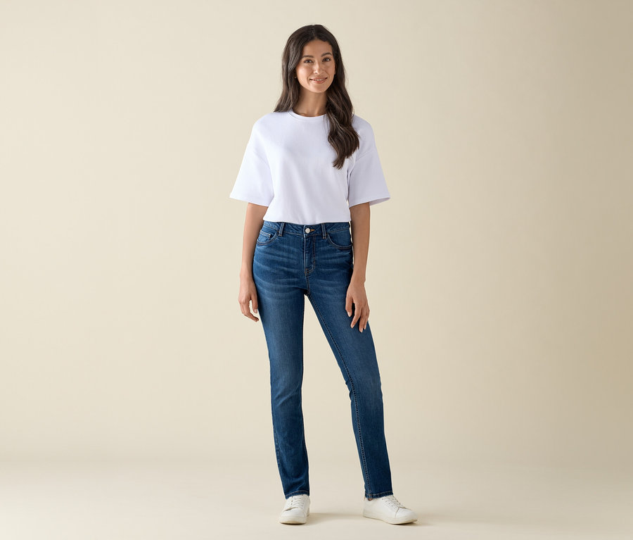 Eine Frau steht und trägt eine Slim-Jeans – Fit »Emma« in Mid Blue Denim und ein weißes T-Shirt.