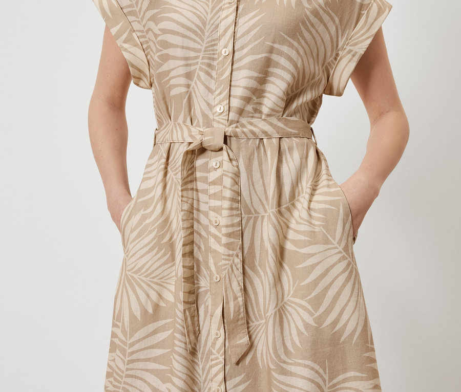 Frau posiert in einem bedruckten Leinenkleid mit Blättermuster und Händen in den Taschen.