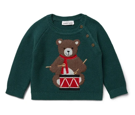 Grüner Pullover mit einem braunen Bären, der mit einem roten Schal auf einer Trommel spielt.