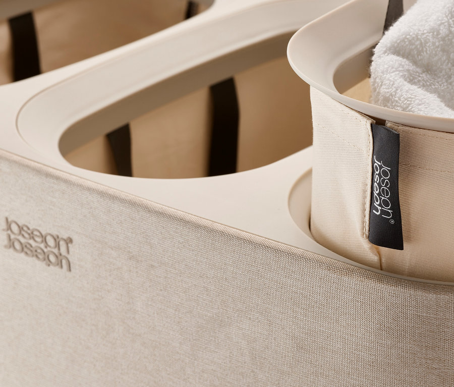 Detailansicht eines beigen Wäschekorbs mit drei Fächern und einem weißen Handtuch in einem davon.