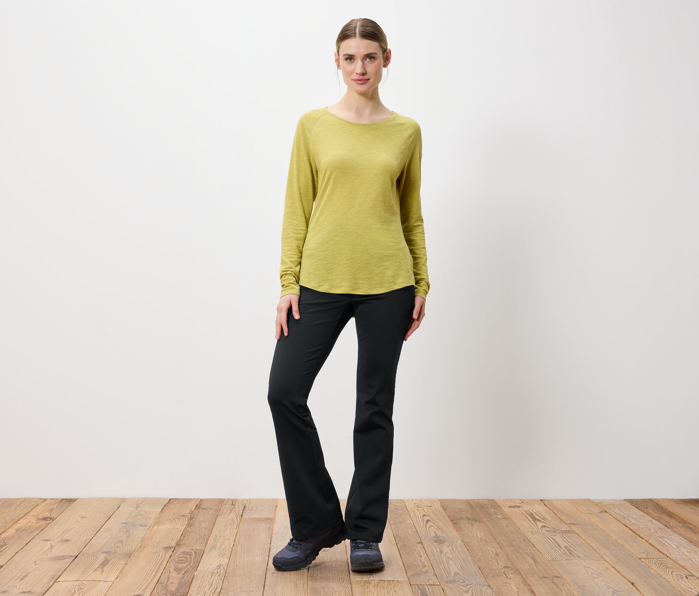 Frau posiert in hellgrünem Langarmshirt und schwarzen Hosen.