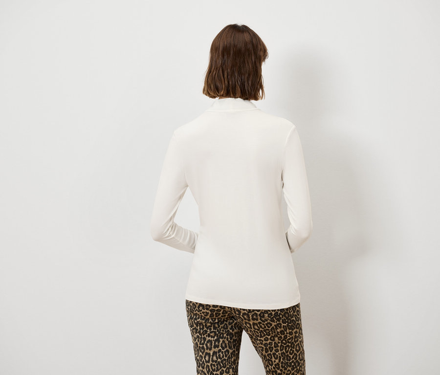 Rückansicht einer Frau mit braunen Haaren, die ein cremefarbenes Langarmshirt und Leopardenhose trägt.