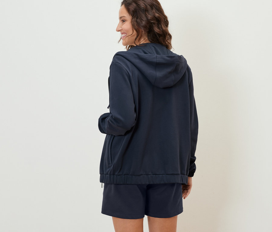 Frau von hinten trägt eine dunkelblaue Sweatjacke und Shorts.