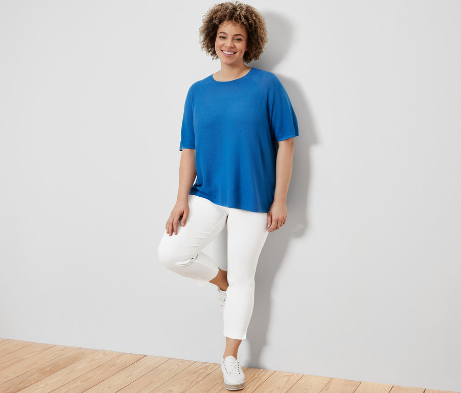 Frau posiert in Feinstrick-Shirt, kobaltblau und 7/8-Stretchhose, weiß.