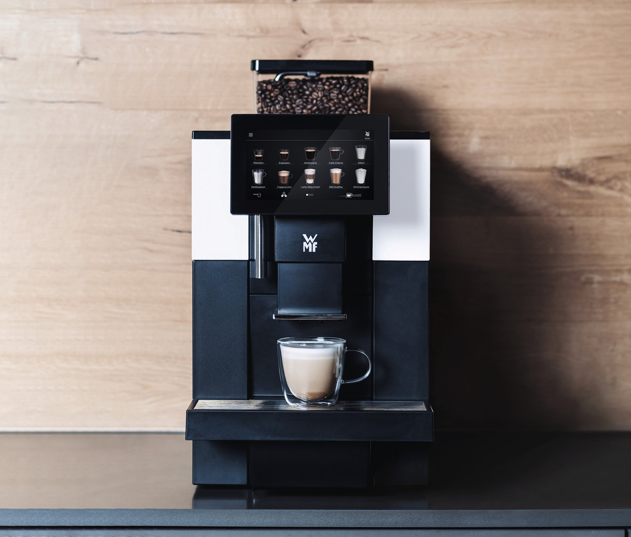 Profi-Kaffeevollautomat »WMF 950 S« vor einer Holzwand. Auf einem Regal darüber befinden sich zwei Blumentöpfe und Tassen.