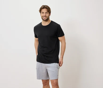 Mann mit schwarzem T-Shirt und grauen Shorts vor einem weißen Hintergrund.
