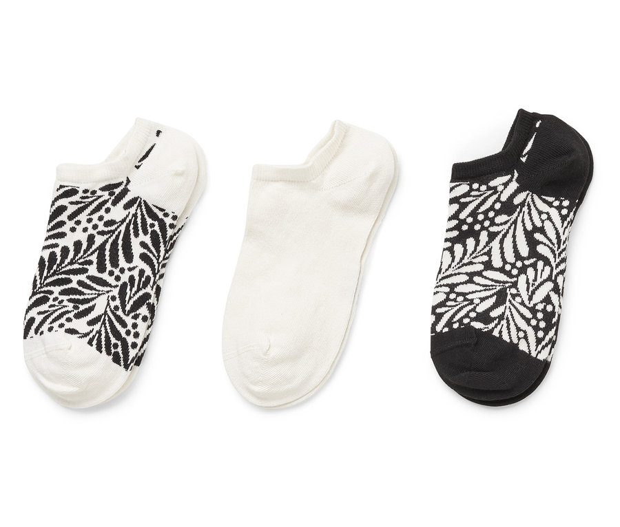 Drei Socken liegen nebeneinander: eine weiße Socke mit schwarzem Blattmuster, eine weiße Socke und eine schwarze Socke mit weißem Blattmuster.