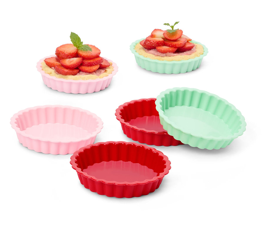Mehrere farbige Tarteformen, einige mit Erdbeertörtchen gefüllt.