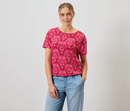 Frau trägt ein rotes, gemustertes T-Shirt und blaue Jeans.